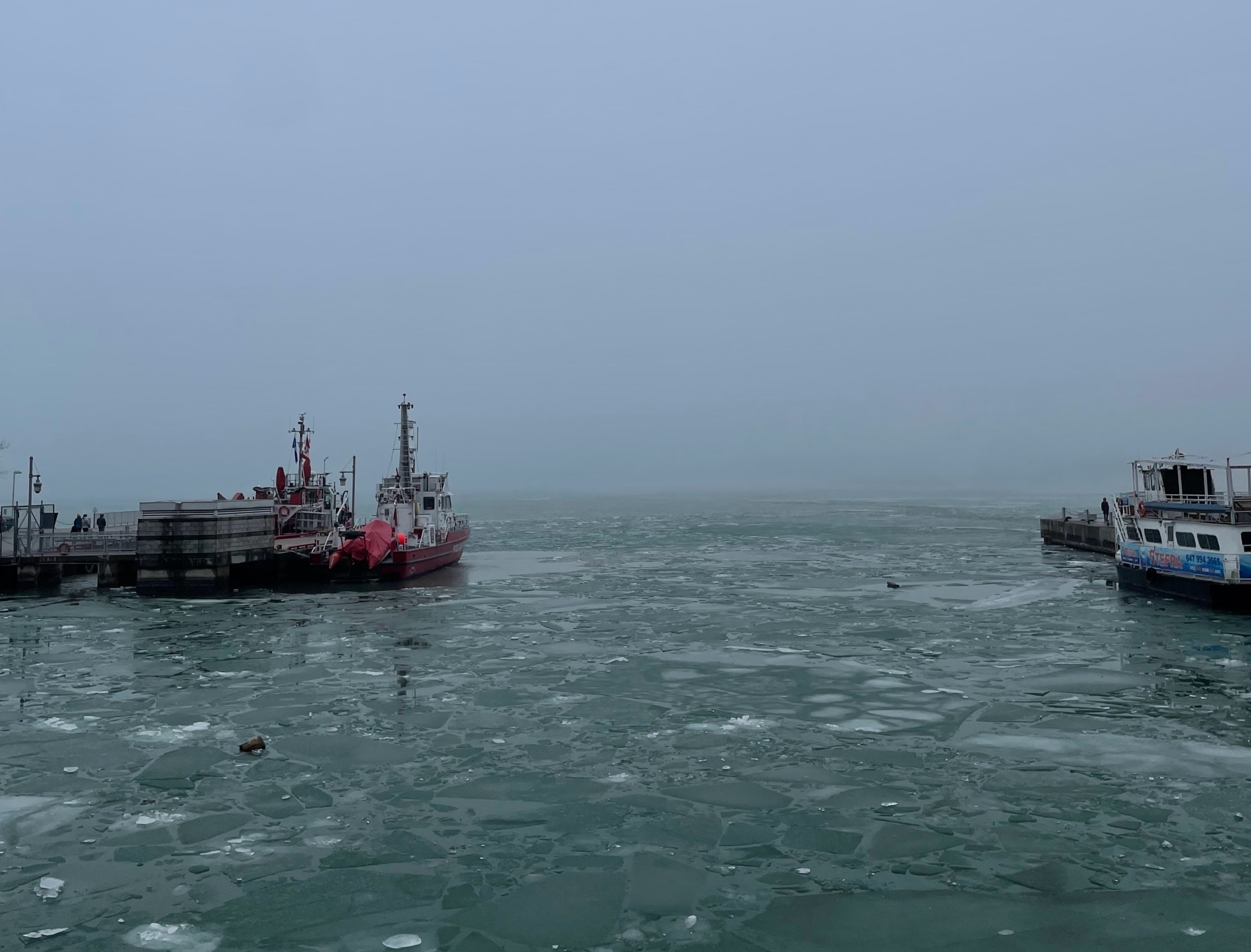 Image of the Harbourfront pier frozen over in Toronto. Mid-day, cloudy, a boat docked on the left.